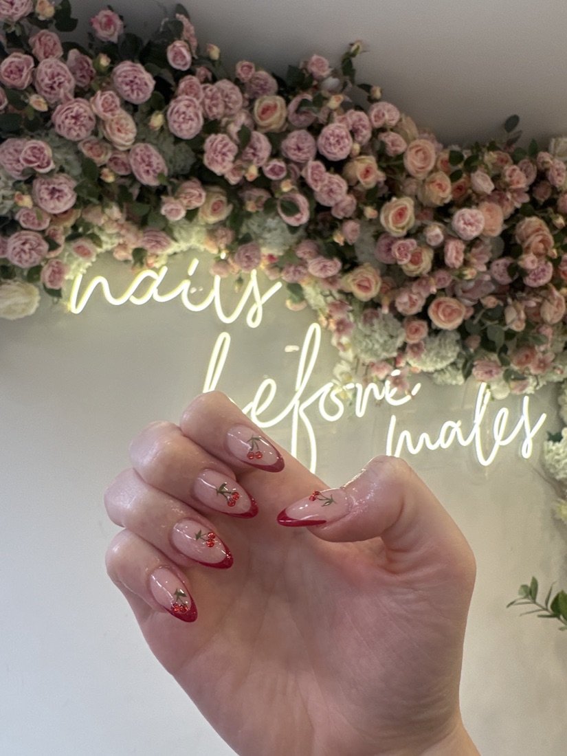 Cherry-red French tips with red-gem cherry art, photographed by the studio's flower wall